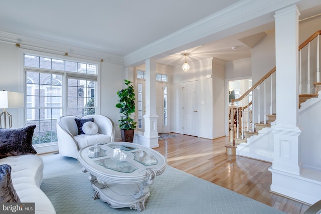 living room featuring baseboards, wood finished floors, stairs, crown molding, and ornate columns