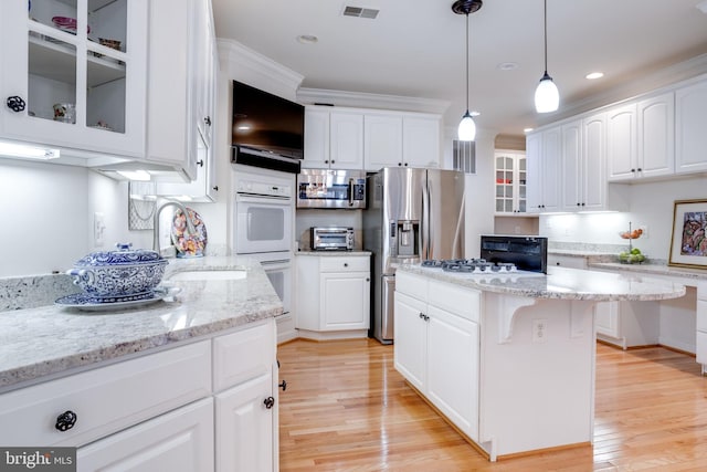 kitchen with a sink, visible vents, light wood-style floors, appliances with stainless steel finishes, and glass insert cabinets