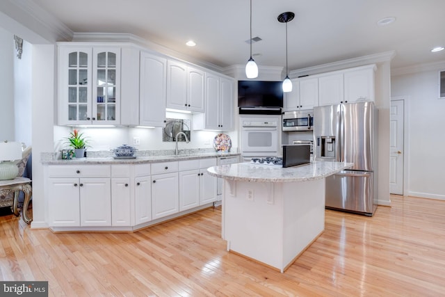 kitchen with appliances with stainless steel finishes, light wood-style floors, glass insert cabinets, white cabinets, and ornamental molding