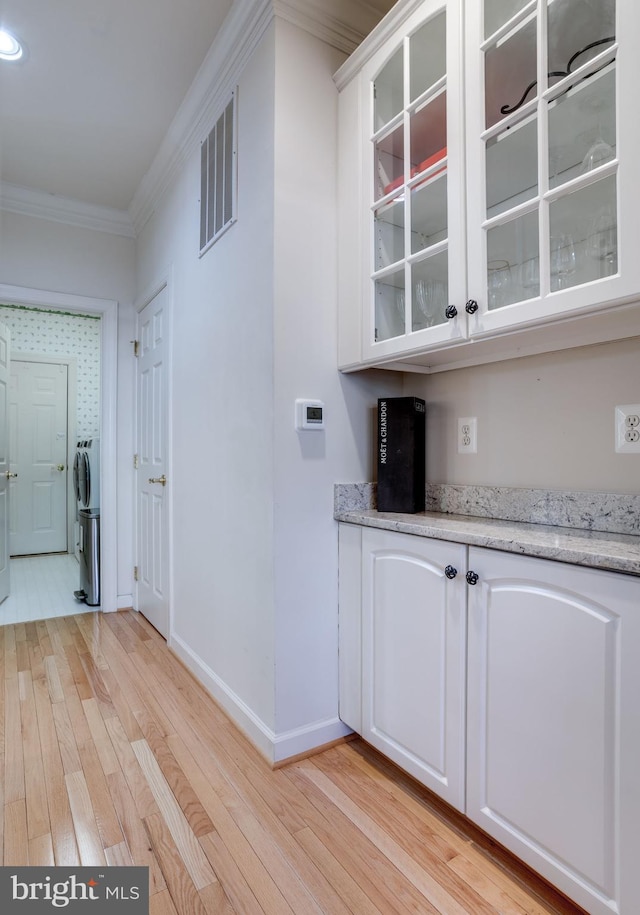 interior space with ornamental molding, visible vents, light wood-style flooring, and baseboards