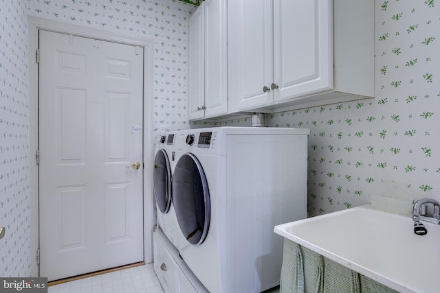 clothes washing area with wallpapered walls, cabinet space, light floors, washing machine and dryer, and a sink