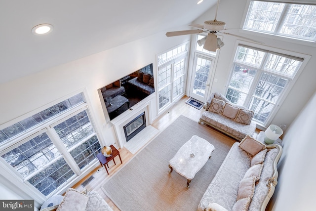 living room with high vaulted ceiling, recessed lighting, a fireplace with flush hearth, wood finished floors, and a ceiling fan