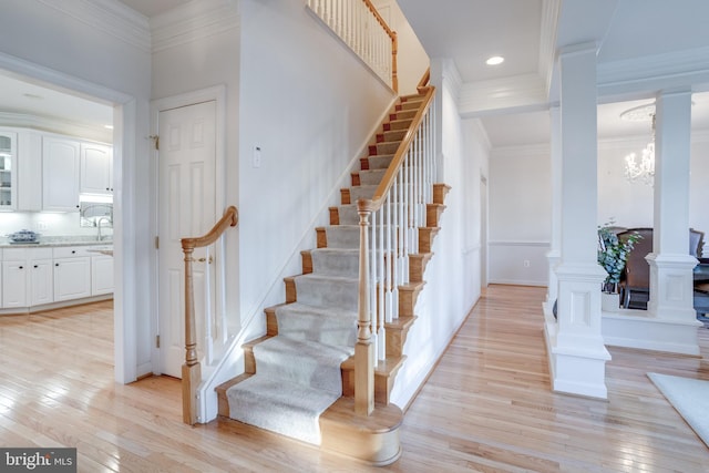 staircase with hardwood / wood-style flooring, decorative columns, ornamental molding, and a chandelier