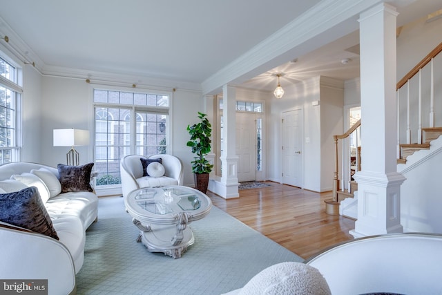 living room featuring baseboards, light wood-style floors, ornamental molding, stairway, and ornate columns