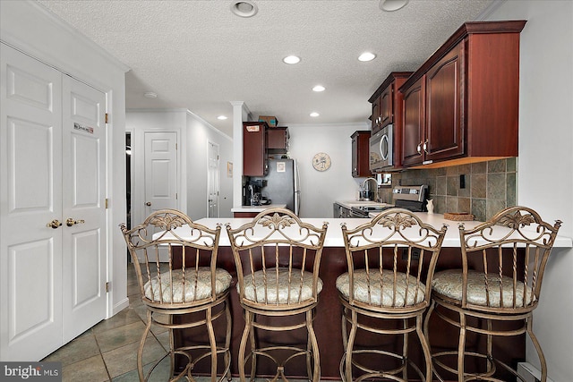 kitchen with a peninsula, light countertops, appliances with stainless steel finishes, decorative backsplash, and crown molding