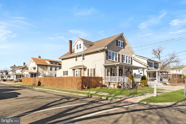 american foursquare style home with a porch, a residential view, fence, and a chimney