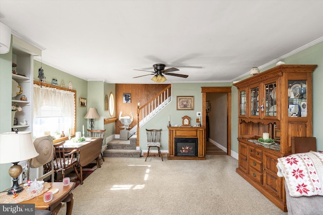 carpeted living room with ceiling fan, stairway, a glass covered fireplace, and ornamental molding