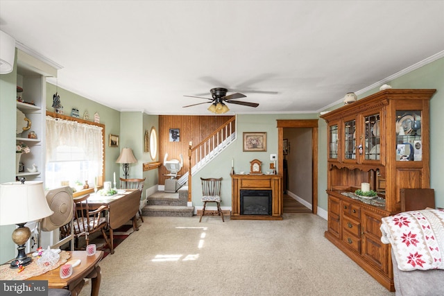 carpeted living area featuring ornamental molding, a glass covered fireplace, ceiling fan, and stairs