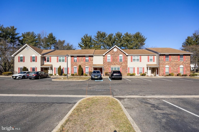 view of property with uncovered parking, brick siding, and a residential view