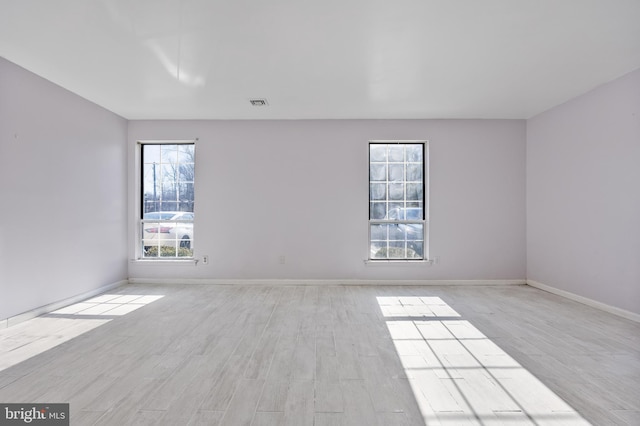 spare room featuring light wood-style floors, visible vents, and baseboards