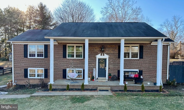 bi-level home with covered porch, brick siding, a front lawn, and fence