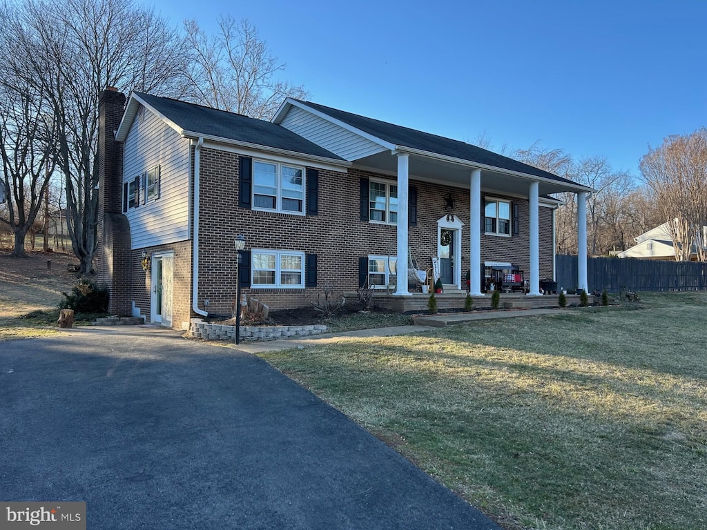 split foyer home featuring a front yard, a chimney, fence, and brick siding