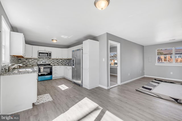 kitchen with stainless steel appliances, decorative backsplash, light wood-style floors, open floor plan, and light stone countertops