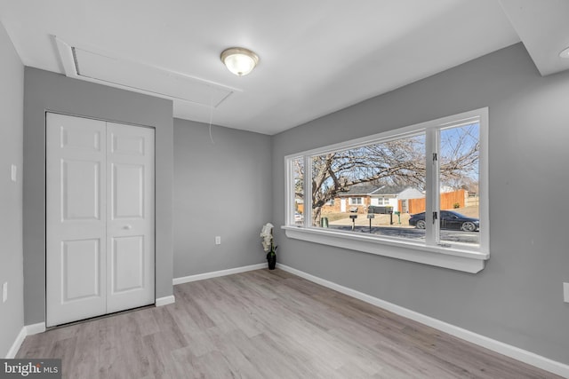 unfurnished bedroom with attic access, a closet, baseboards, and wood finished floors