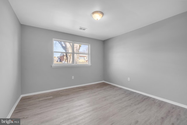 spare room with baseboards, visible vents, and wood finished floors