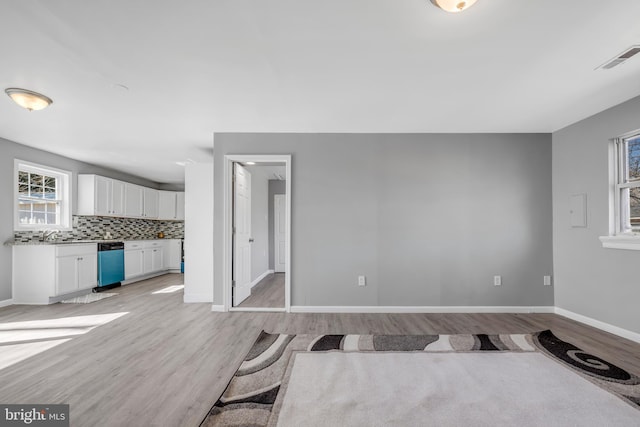 unfurnished living room with light wood finished floors, visible vents, and baseboards