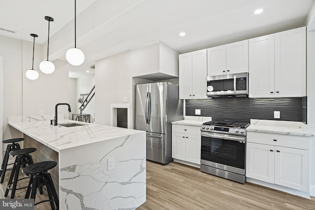 kitchen with visible vents, a kitchen breakfast bar, stainless steel appliances, light wood-type flooring, and a sink