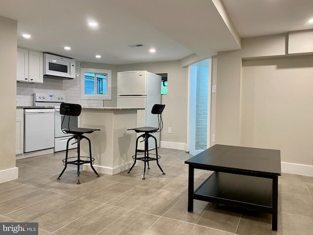 kitchen with tasteful backsplash, visible vents, white cabinetry, white appliances, and a kitchen breakfast bar