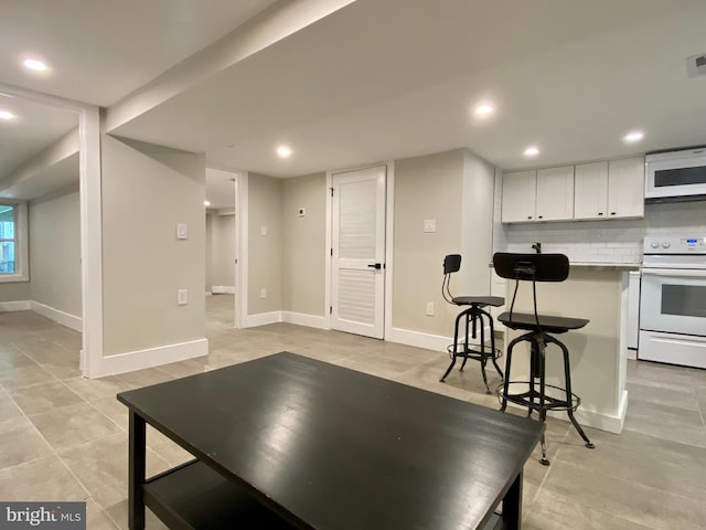 kitchen with a breakfast bar area, white appliances, baseboards, white cabinets, and decorative backsplash