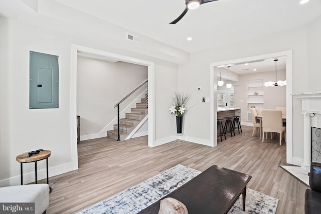 living area with visible vents, light wood-style flooring, ceiling fan, electric panel, and stairs