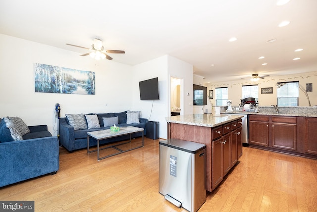 kitchen featuring ceiling fan, light wood-style flooring, light stone counters, open floor plan, and a center island