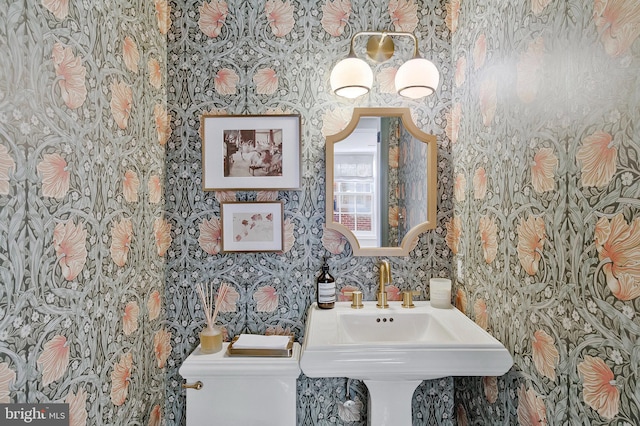 half bath featuring a sink, toilet, and wallpapered walls