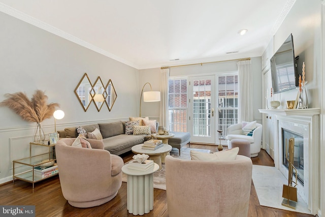 living area with dark wood-style flooring, a fireplace, crown molding, and a wainscoted wall