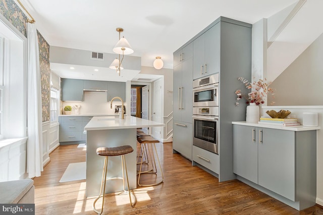 kitchen with gray cabinets, visible vents, light wood-style floors, a sink, and a kitchen breakfast bar