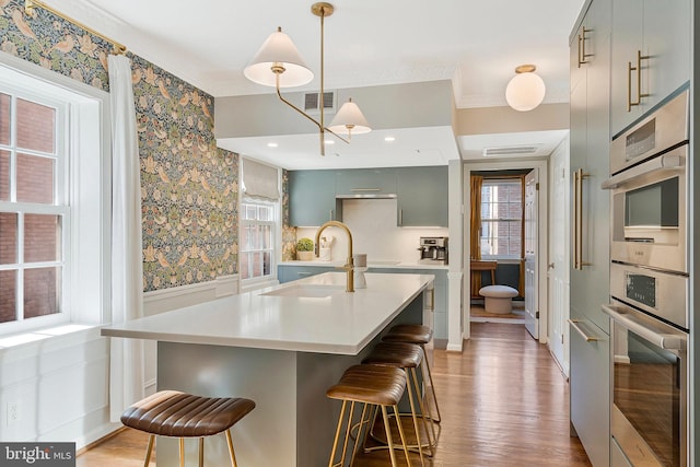 kitchen featuring a sink, visible vents, light wood-style floors, light countertops, and wallpapered walls