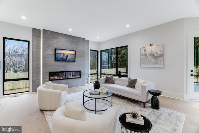 living room with light wood-style floors, a large fireplace, plenty of natural light, and baseboards