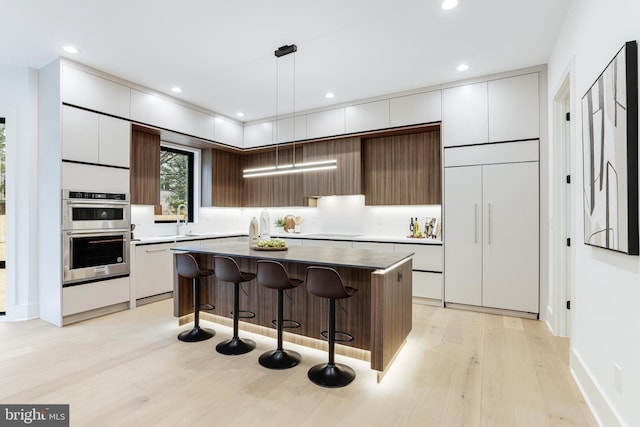 kitchen with stainless steel double oven, a kitchen island, paneled built in fridge, modern cabinets, and a kitchen bar