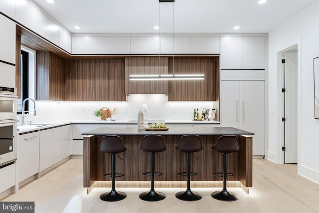 kitchen featuring white cabinets, modern cabinets, a breakfast bar, a center island, and a sink