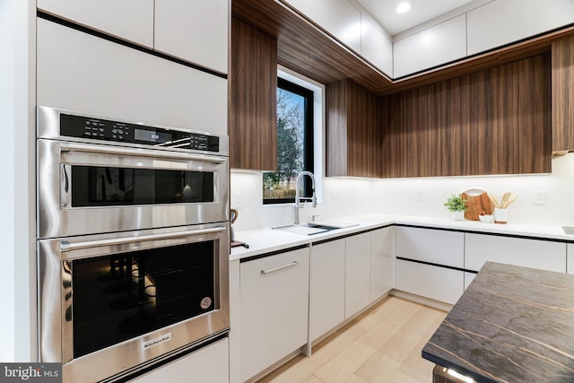 kitchen featuring modern cabinets, light countertops, stainless steel double oven, white cabinetry, and a sink