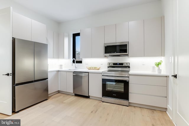 kitchen featuring a sink, light countertops, appliances with stainless steel finishes, light wood finished floors, and tasteful backsplash