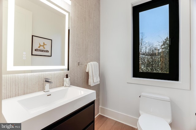 bathroom with toilet, wood finished floors, vanity, and baseboards