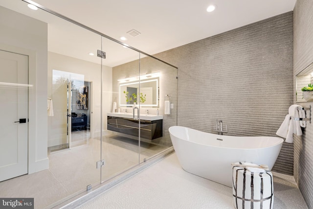 bathroom with a freestanding tub, vanity, tile walls, and recessed lighting