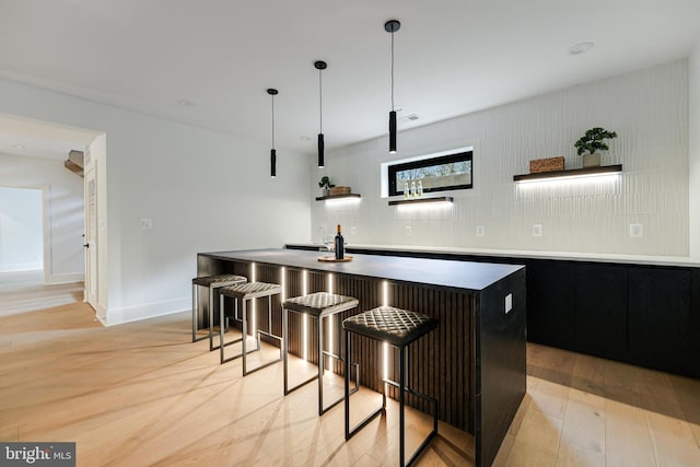 bar with indoor wet bar, decorative light fixtures, light wood finished floors, backsplash, and baseboards