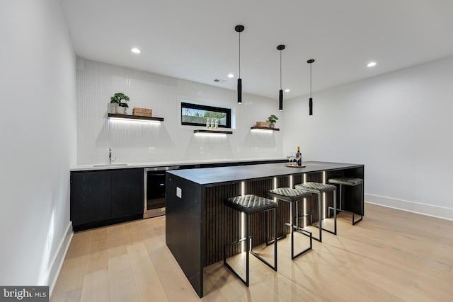 bar with light wood-style floors, wine cooler, indoor wet bar, and a sink