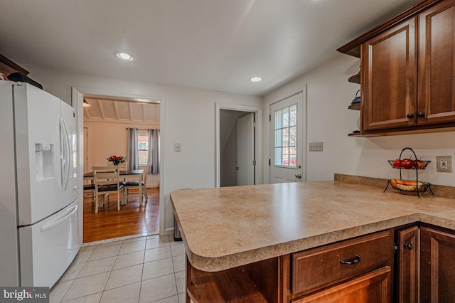 kitchen with white refrigerator with ice dispenser, light tile patterned floors, open shelves, light countertops, and a peninsula