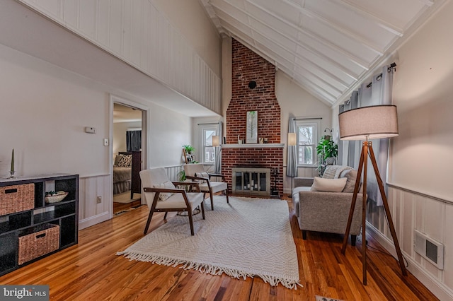 living room featuring visible vents, wainscoting, hardwood / wood-style flooring, a brick fireplace, and beam ceiling