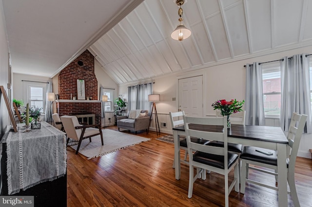 dining space with plenty of natural light, wood-type flooring, a fireplace, and vaulted ceiling