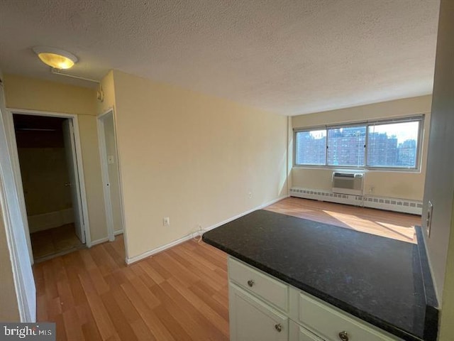 kitchen featuring dark countertops, baseboard heating, light wood-style floors, white cabinetry, and a textured ceiling