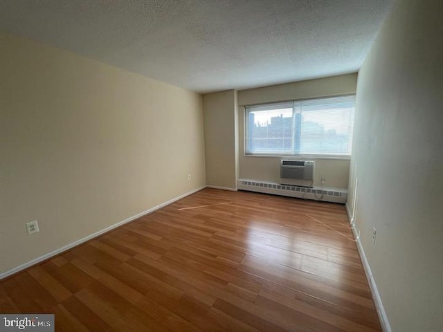 unfurnished room featuring a baseboard heating unit, a textured ceiling, wood finished floors, and baseboards