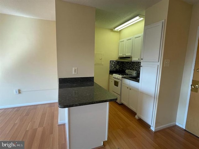 kitchen with white gas stove, a peninsula, white cabinets, light wood-type flooring, and backsplash