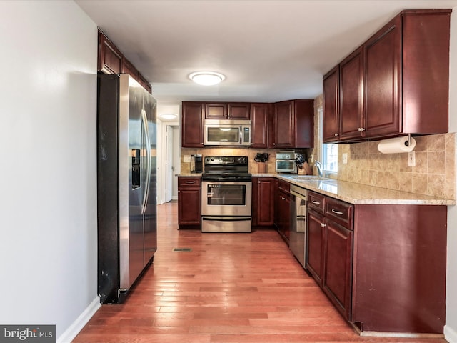 kitchen featuring decorative backsplash, appliances with stainless steel finishes, a sink, light wood-type flooring, and baseboards