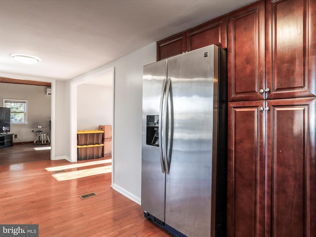 kitchen with light wood finished floors, stainless steel refrigerator with ice dispenser, visible vents, and baseboards