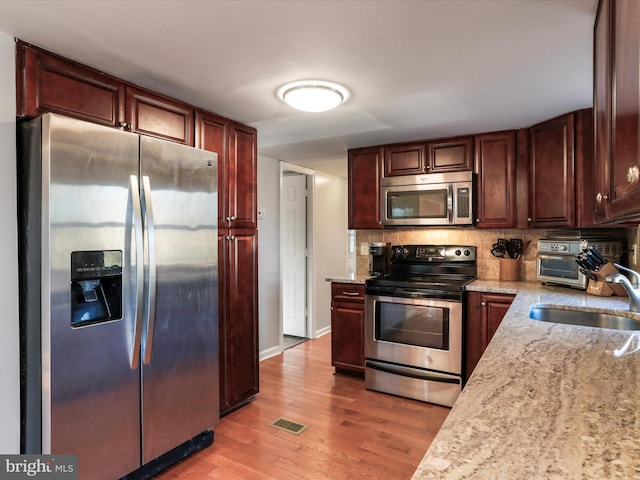 kitchen with tasteful backsplash, light stone counters, stainless steel appliances, light wood-type flooring, and a sink