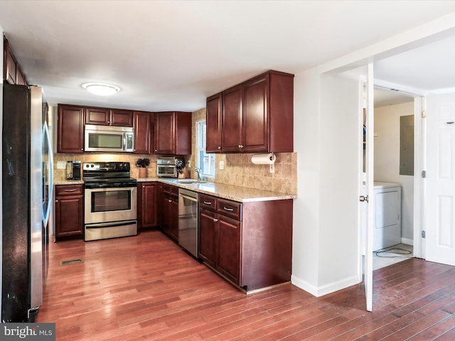 kitchen with washer / clothes dryer, backsplash, appliances with stainless steel finishes, a sink, and light wood-type flooring