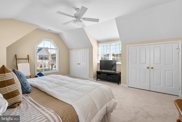 bedroom featuring multiple closets, lofted ceiling, a ceiling fan, baseboards, and light colored carpet