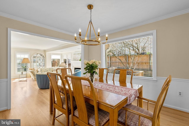 dining area with a wainscoted wall, crown molding, and light wood-style floors